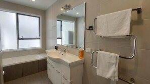 A modern bathroom with a large mirror, a sink, and two towel racks. - Seaview Garden House Close to Beach (Auckland)