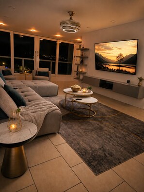 Una sala de estar moderna con un sofá grande, dos mesitas auxiliares, una chimenea y un televisor de gran tamaño en la pared.