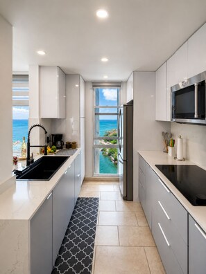 Una cocina moderna con vista al océano, microondas integrado y refrigerador de acero inoxidable.