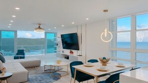 A modern living room with a large TV, comfortable seating, and a view of the sea. - Caribbean Dream Condo – Oceanfront, Mountain Views & Modern Comfort (Fajardo)