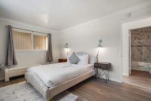 Ein Schlafzimmer mit einem großen Bett, Nachttischen, einer Bank und einem Badezimmer mit Dusche und Toilette.