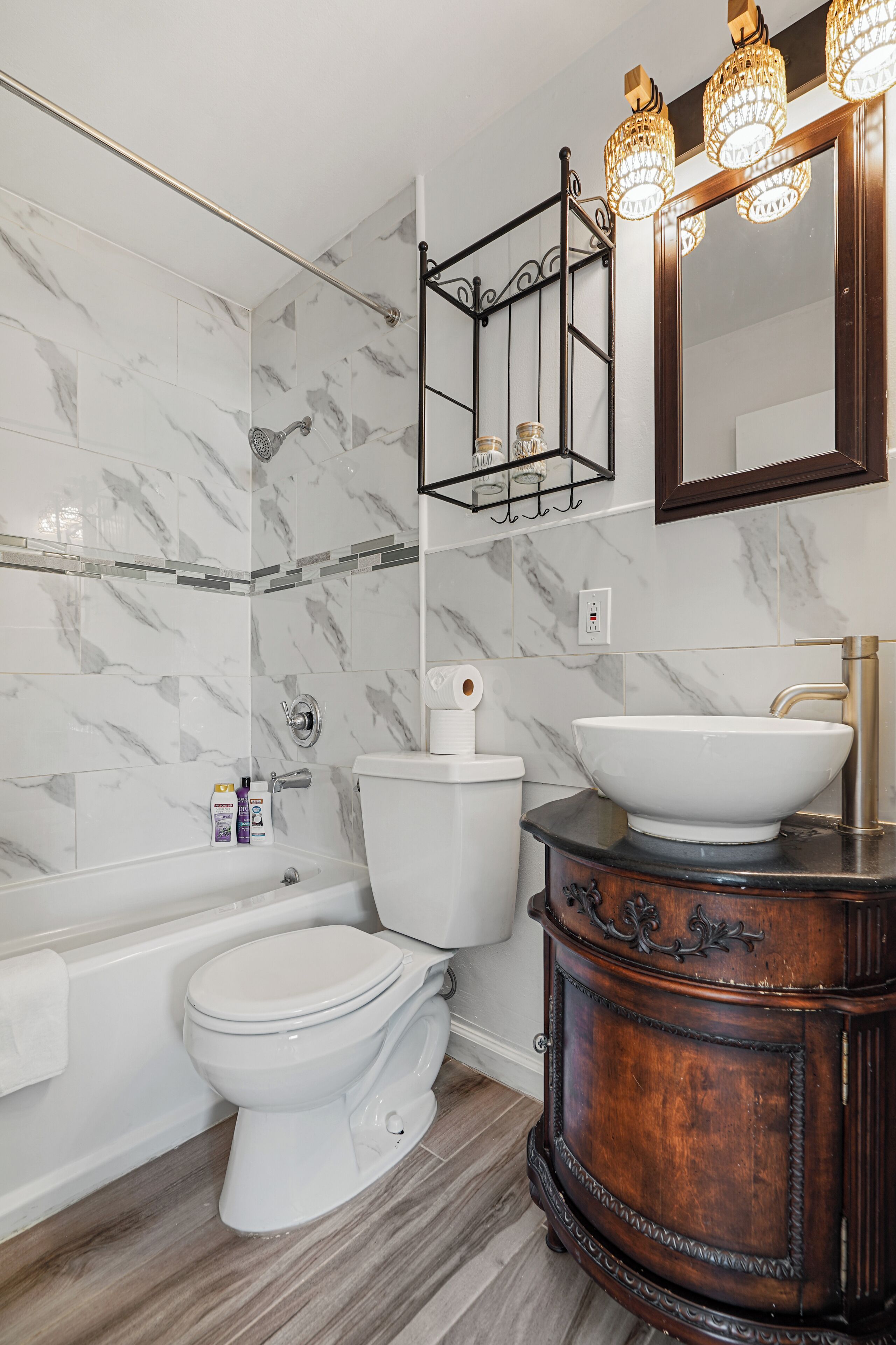 A bathroom with a marble shower wall, a freestanding bathtub, a white toilet, a vanity with a sink, and a mirror.