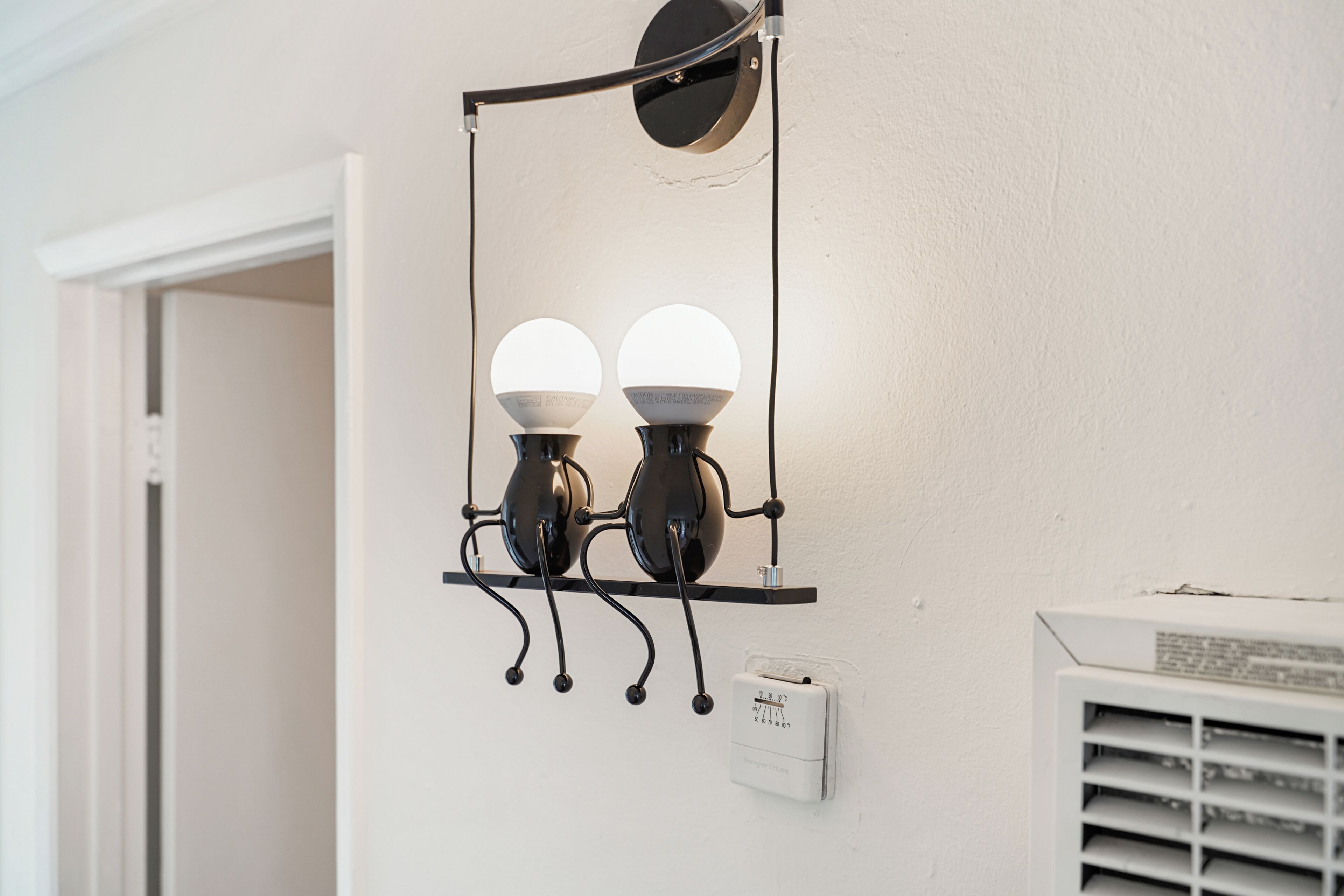 A wall-mounted light fixture with two spherical bulbs and a thermostat.