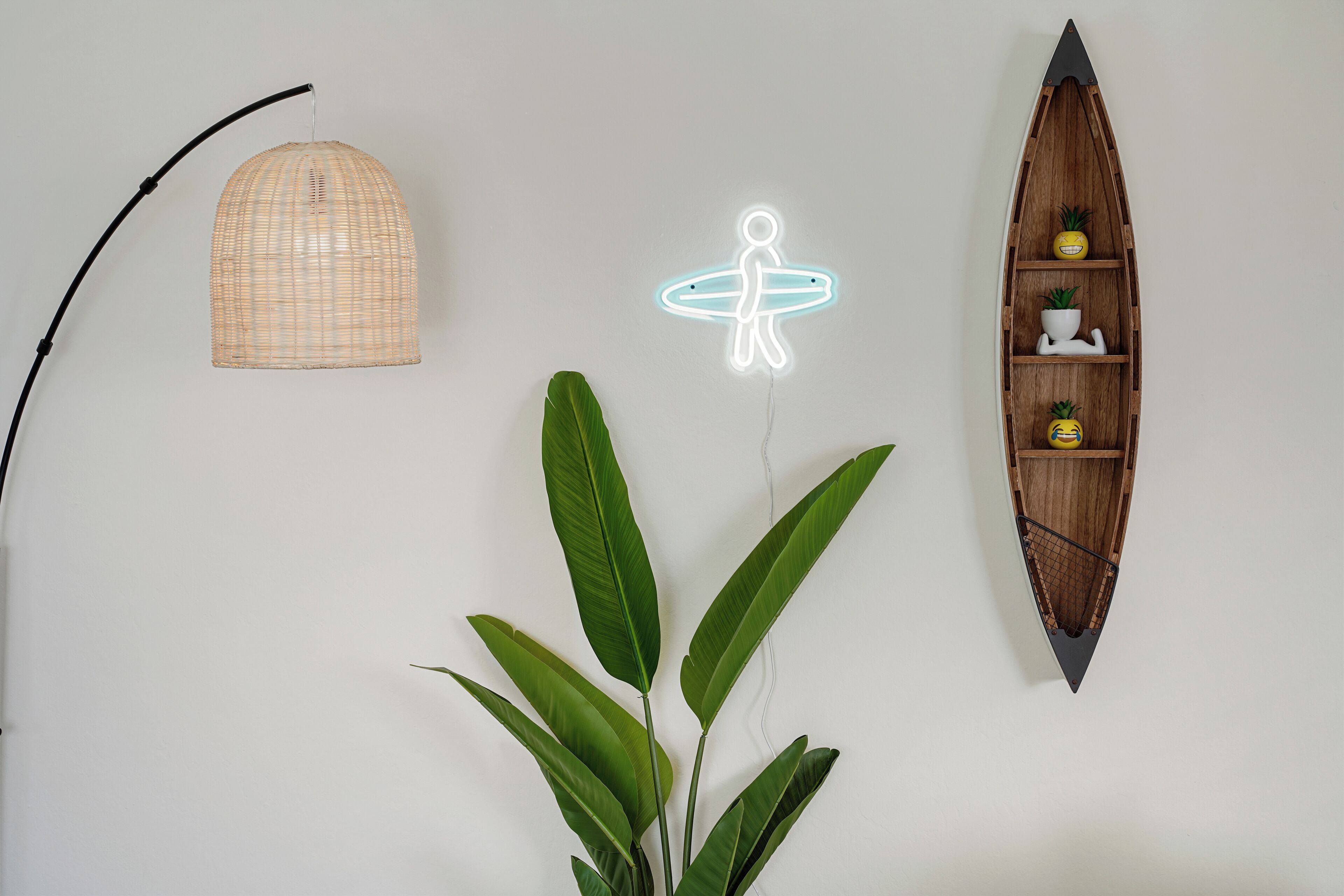 A wall with a hanging wicker lamp, a neon surfboard sign, a wooden boat shelf, and a potted plant.