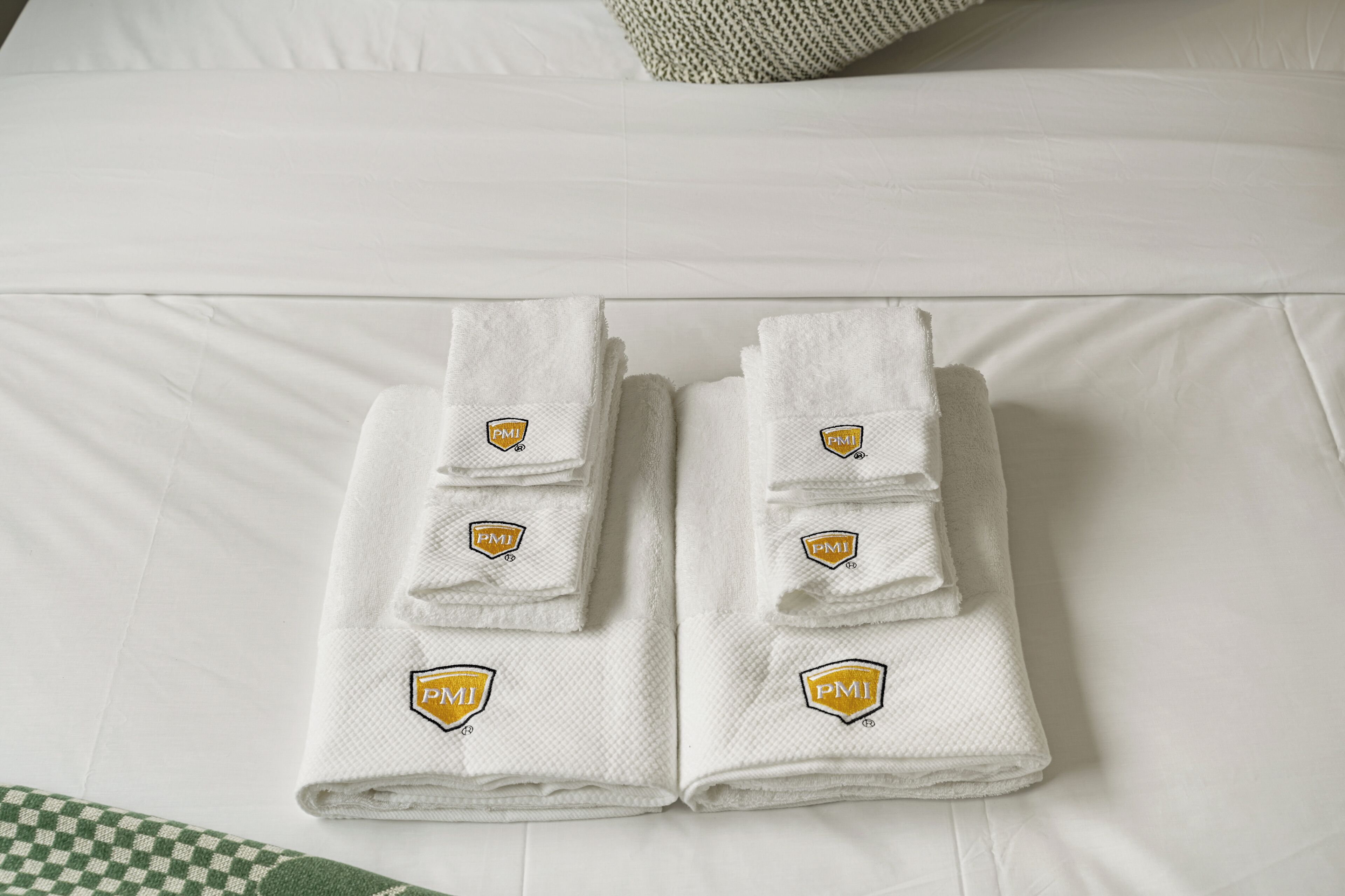 A neatly folded set of white towels with a logo on a bed.