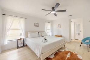A bedroom with a bed, a ceiling fan, a nightstand, a dresser, a cowhide rug, and a blue chair.