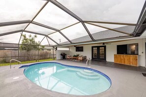 A covered swimming pool with a patio area, a grill, and a seating arrangement.