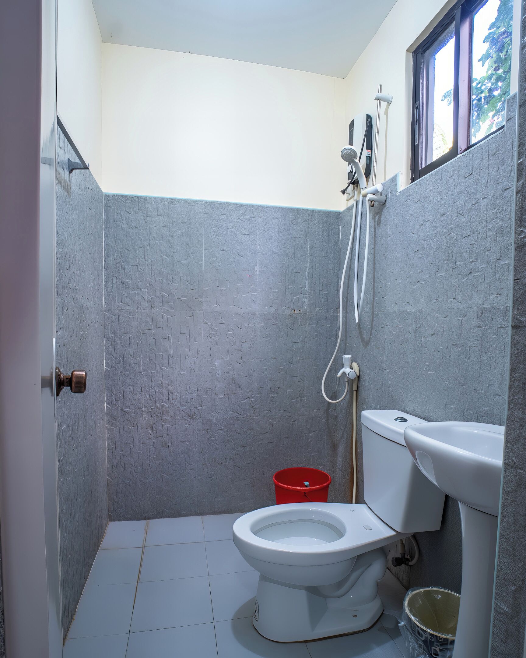 Un baño pequeño con un inodoro, un cubo rojo y una ducha.