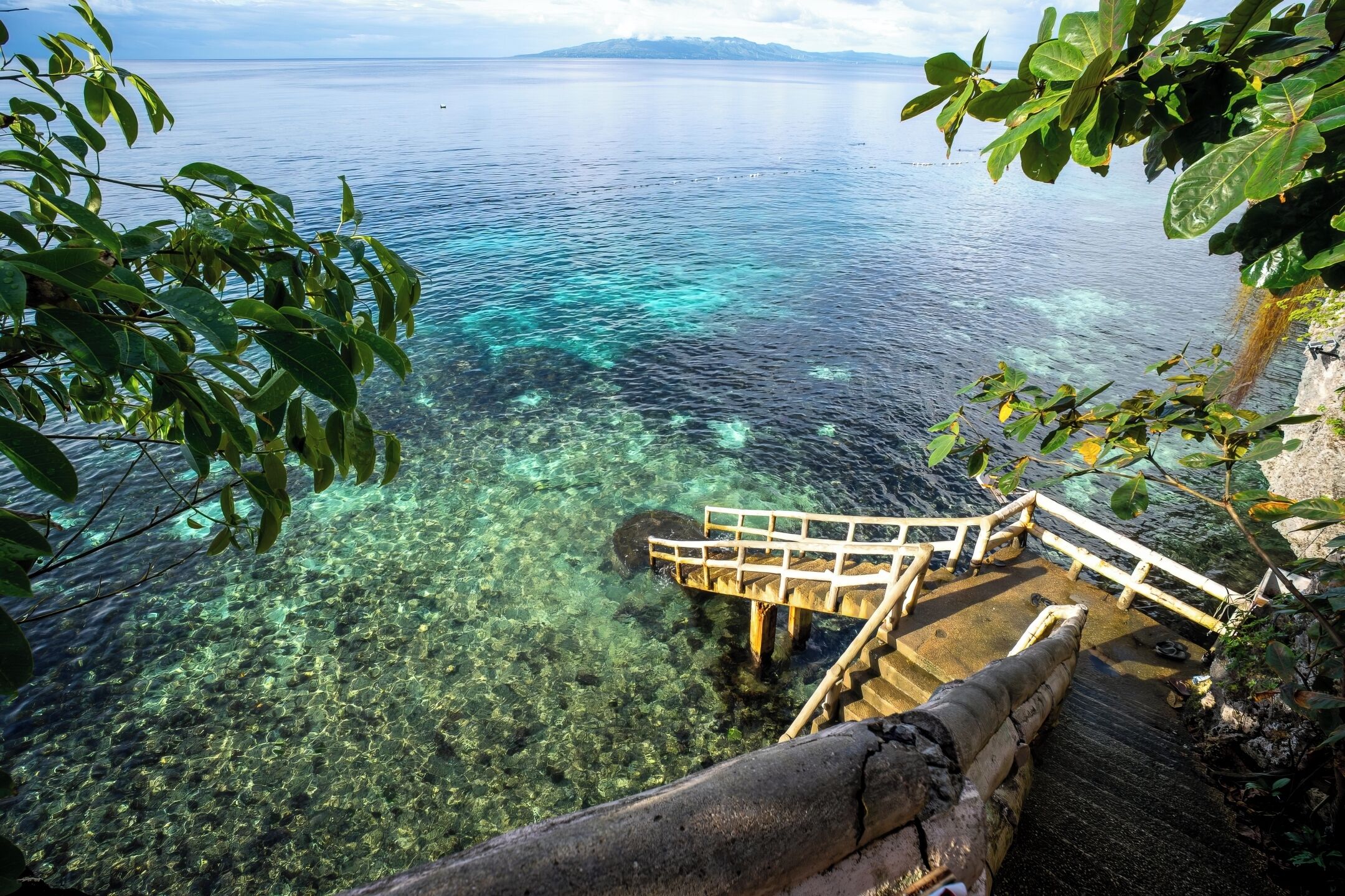 Una escalera de madera que desciende hacia una masa de agua azul cristalina, con una vista distante de montañas.
