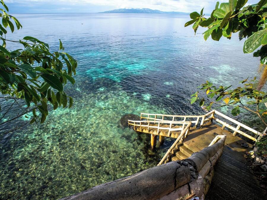 Una escalera de madera que desciende hacia una masa de agua azul cristalina, con una vista distante de montañas.