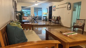 Un salon spacieux avec une table basse en bois, un canapé agrémenté d’un coussin vert et un coin repas comprenant des chaises et une table.