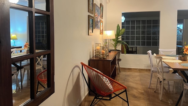 Un coin repas avec une table en bois, des chaises blanches, une chaise rouge, une lampe et des tableaux encadrés accrochés au mur.