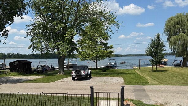 A patio area with a view of a lake, a swing set, and a Jeep parked by the water.
