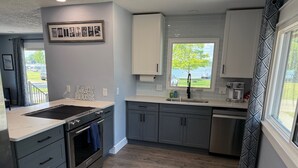 A modern kitchen with grey cabinets, a stainless steel sink, and a window overlooking a lake.
