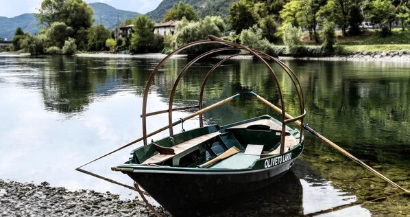 A small green boat with a canopy, docked at a riverbank with a house and trees in the background.