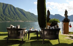 A lakeside terrace with wicker chairs, a table with glasses, and a statue.