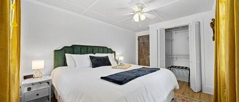 A neatly made bed with a green headboard, a bedside table with a lamp, and a colorful rug on the wooden floor.