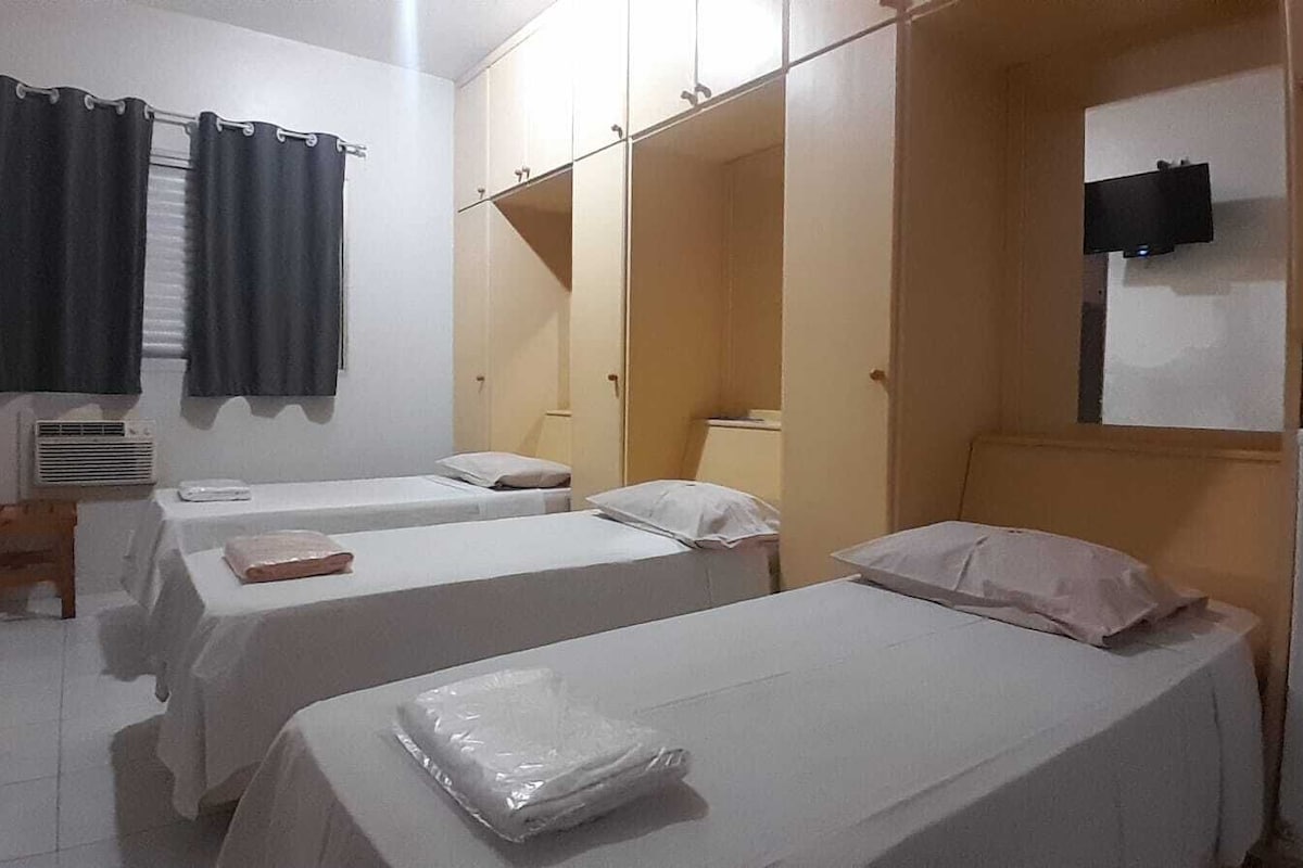 Une chambre d’hôtel avec deux lits simples, une chaise en bois, un téléviseur à écran plat et une armoire.