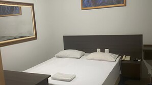 A neatly made bed with pillows, a bedside table, a nightstand, and a framed picture on the wall. - Center plaza hotel (Sao Paulo)