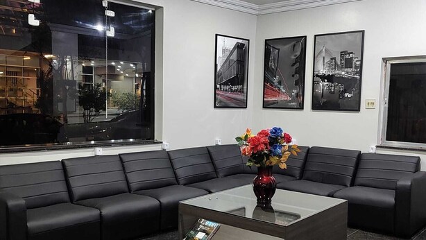 A modern lobby with a black leather sofa, a glass coffee table with magazines, and three black-and-white cityscape photographs on the wall. - Center plaza hotel (Sao Paulo)