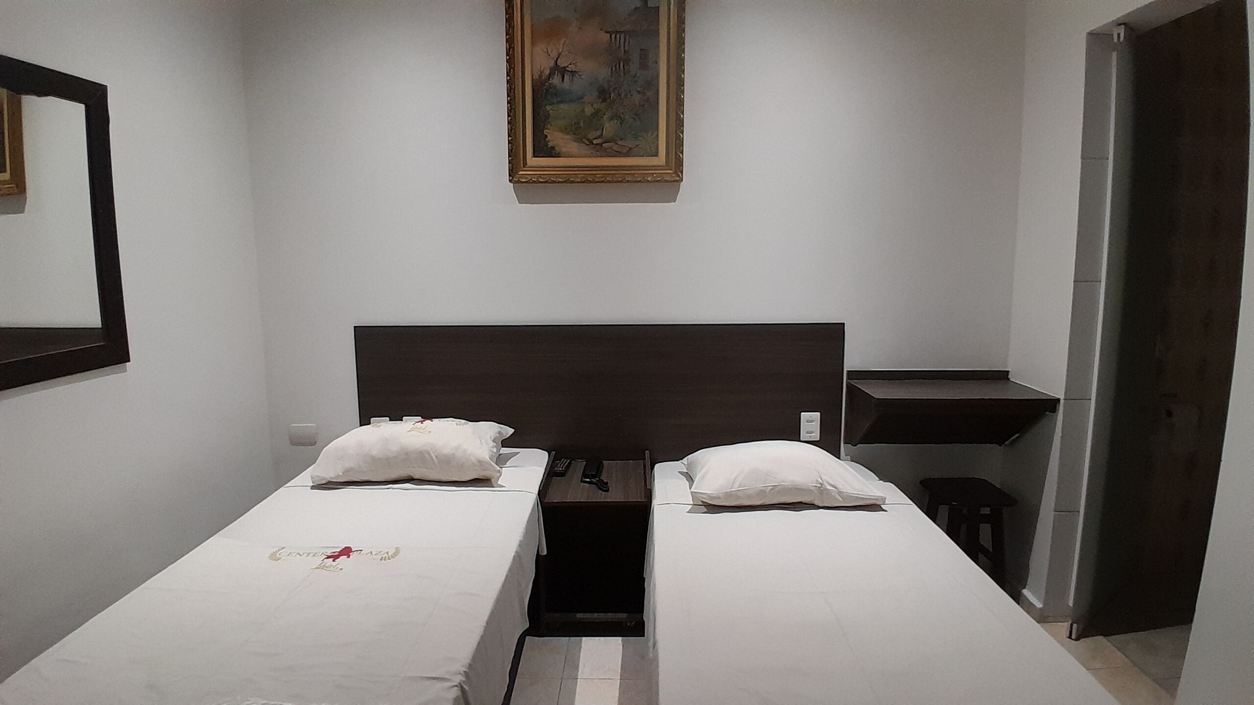 Una habitación sencilla y limpia con una cama, una mesita pequeña y un cuadro en la pared.
