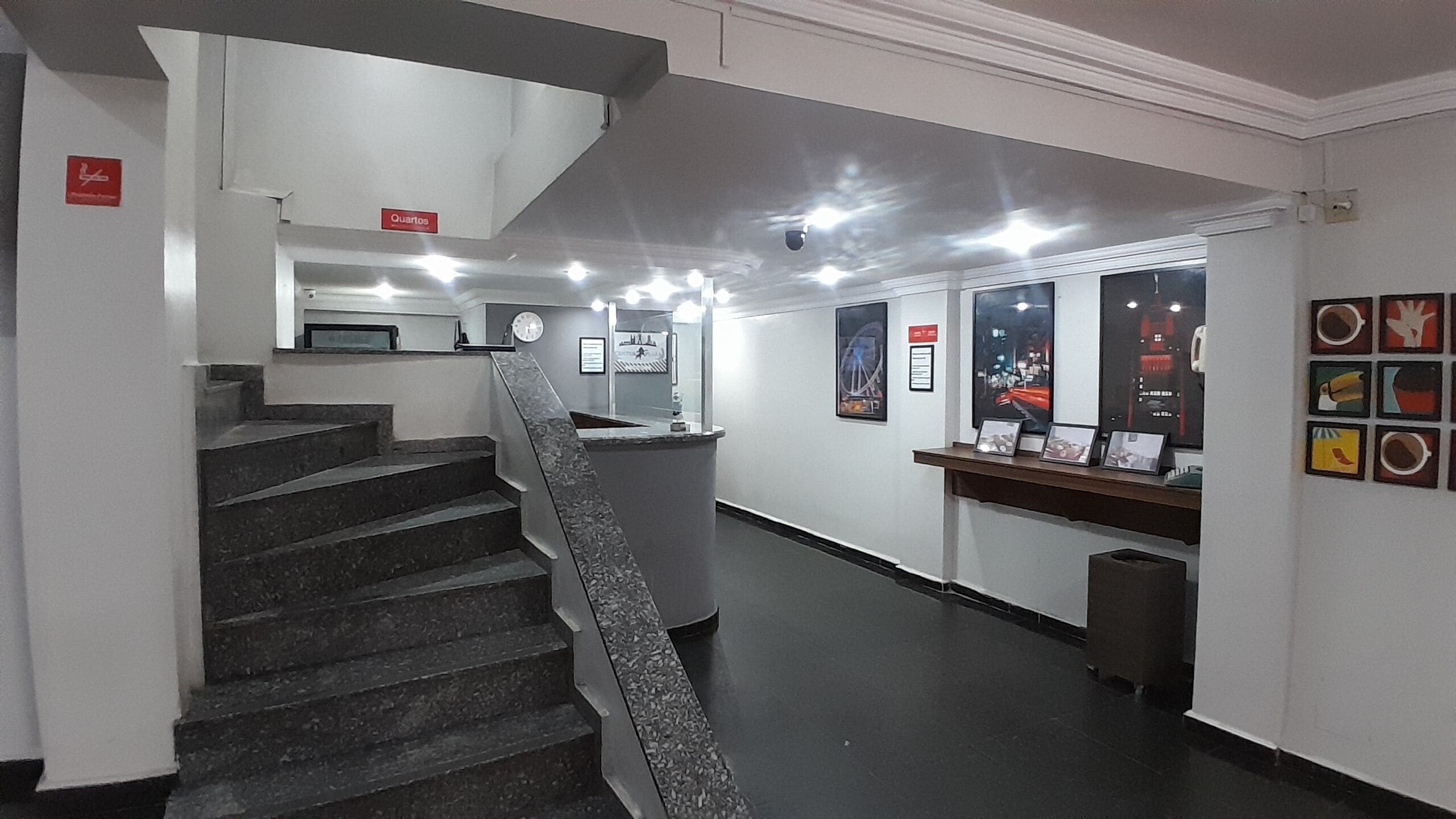 A staircase leading to a reception area with a counter, framed pictures on the wall, and a clock.