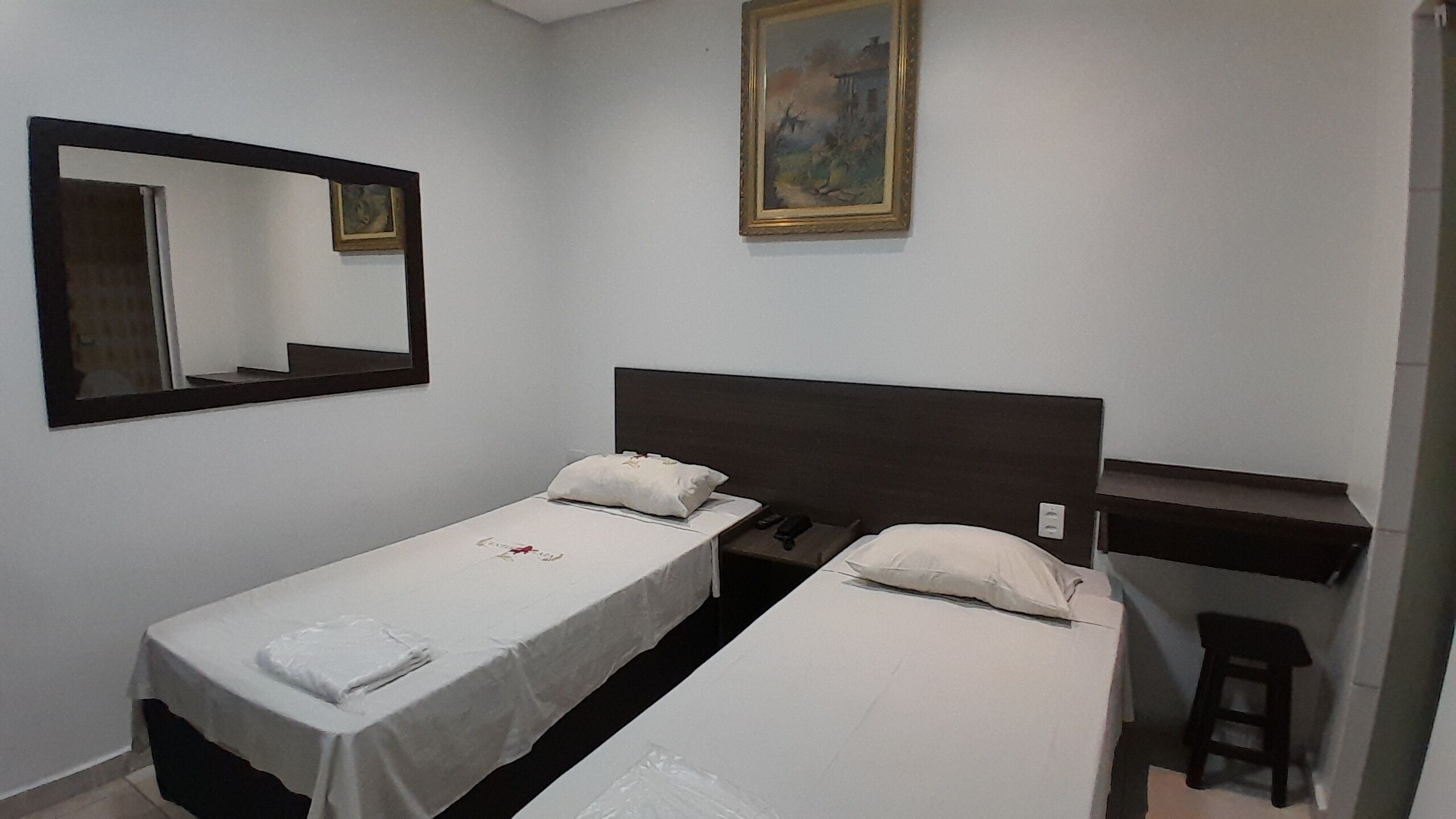 A small, clean room with two single beds, a mirror, and a painting on the wall.