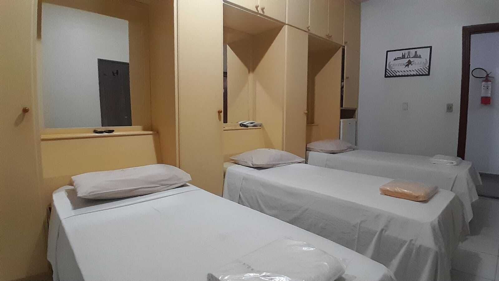 Habitación de hotel con tres camas individuales, un armario de madera, un espejo y un cuadro en la pared.