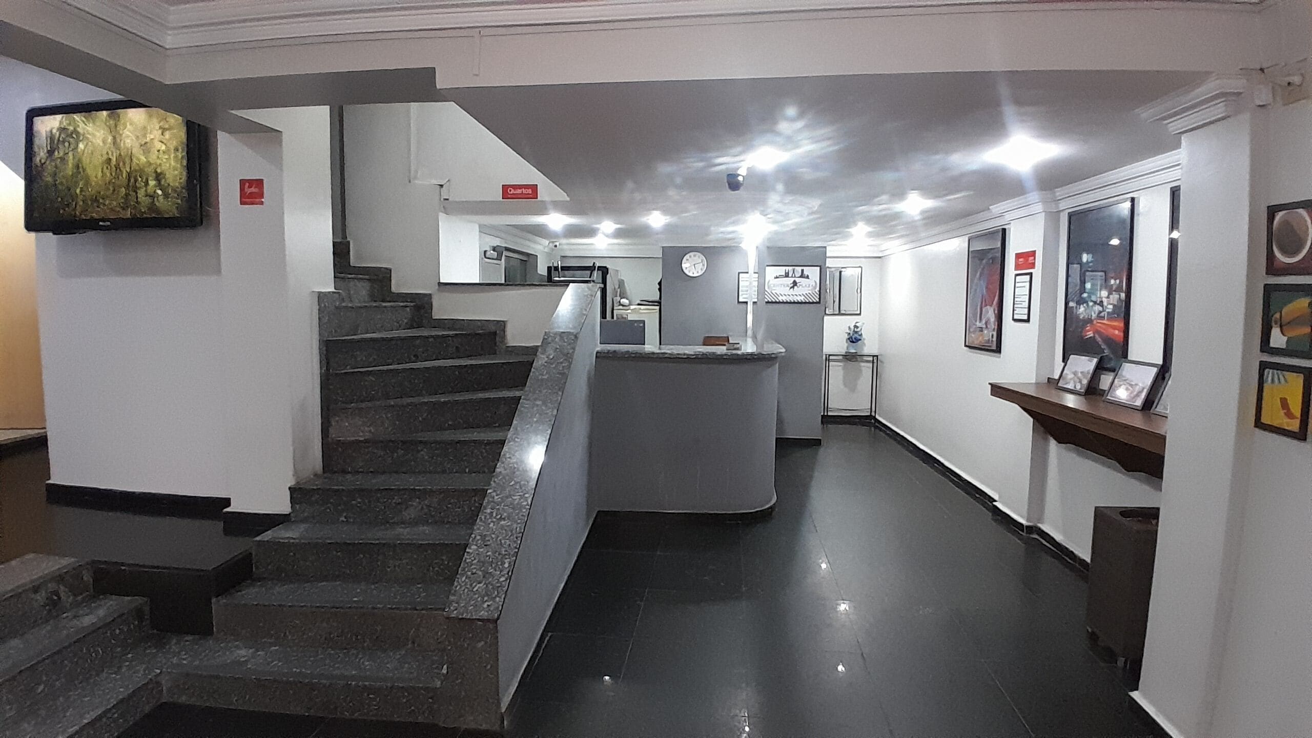 A hotel lobby with a staircase, a reception desk, and a wall-mounted television.