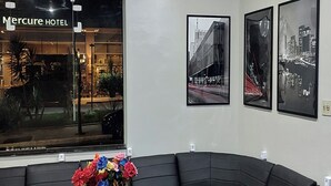 A hotel lobby with a black leather sofa, a glass coffee table, and a vase with colorful flowers. There are three framed pictures on the wall. - Center plaza hotel (Sao Paulo)