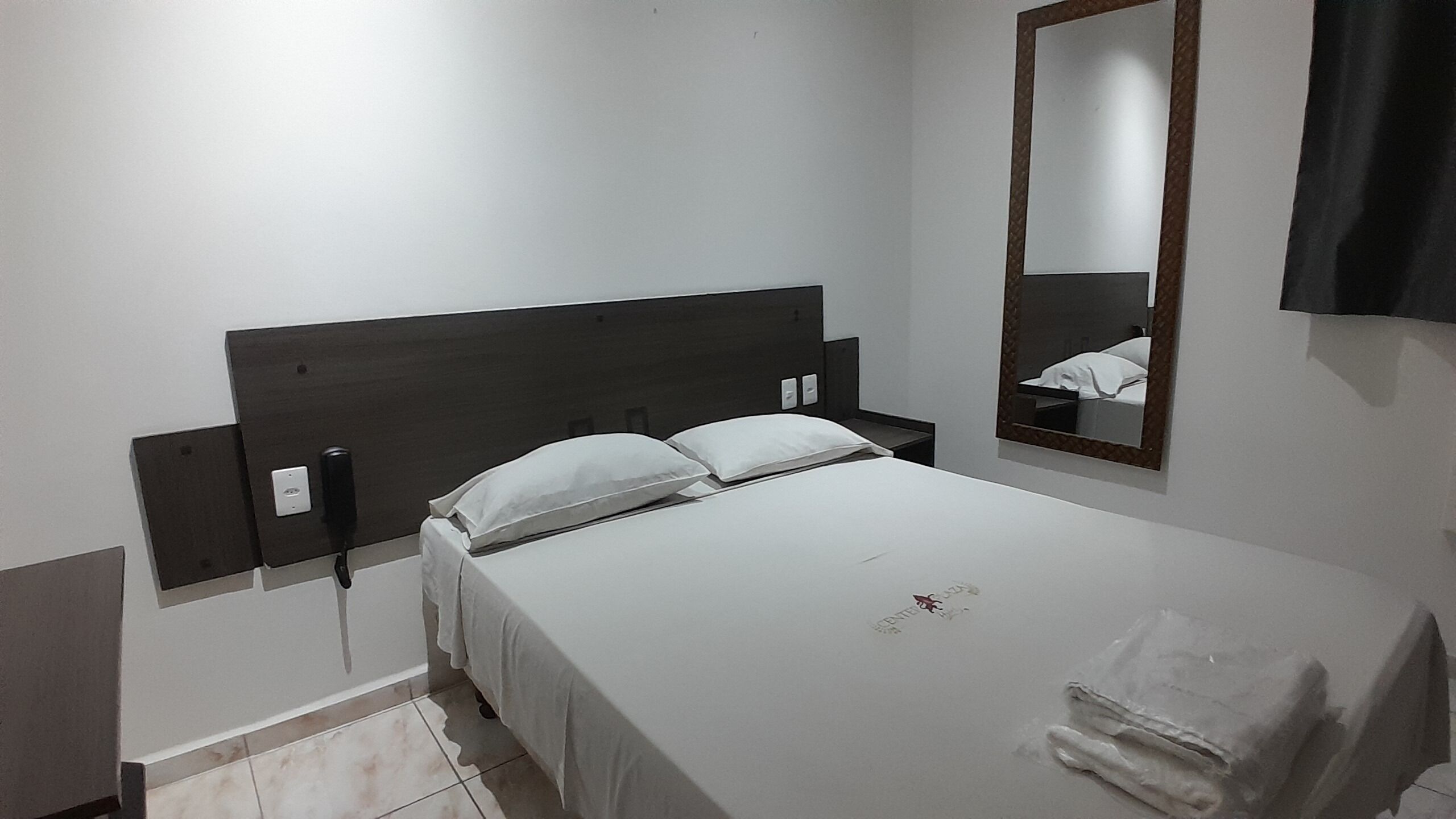 A hotel room with a single bed, a nightstand, a mirror, and a wall-mounted TV.