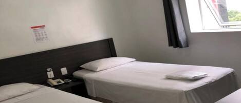 Habitación de hotel con dos camas, una mesita de noche con teléfono y lámpara, una ventana con cortina y un calendario en la pared.