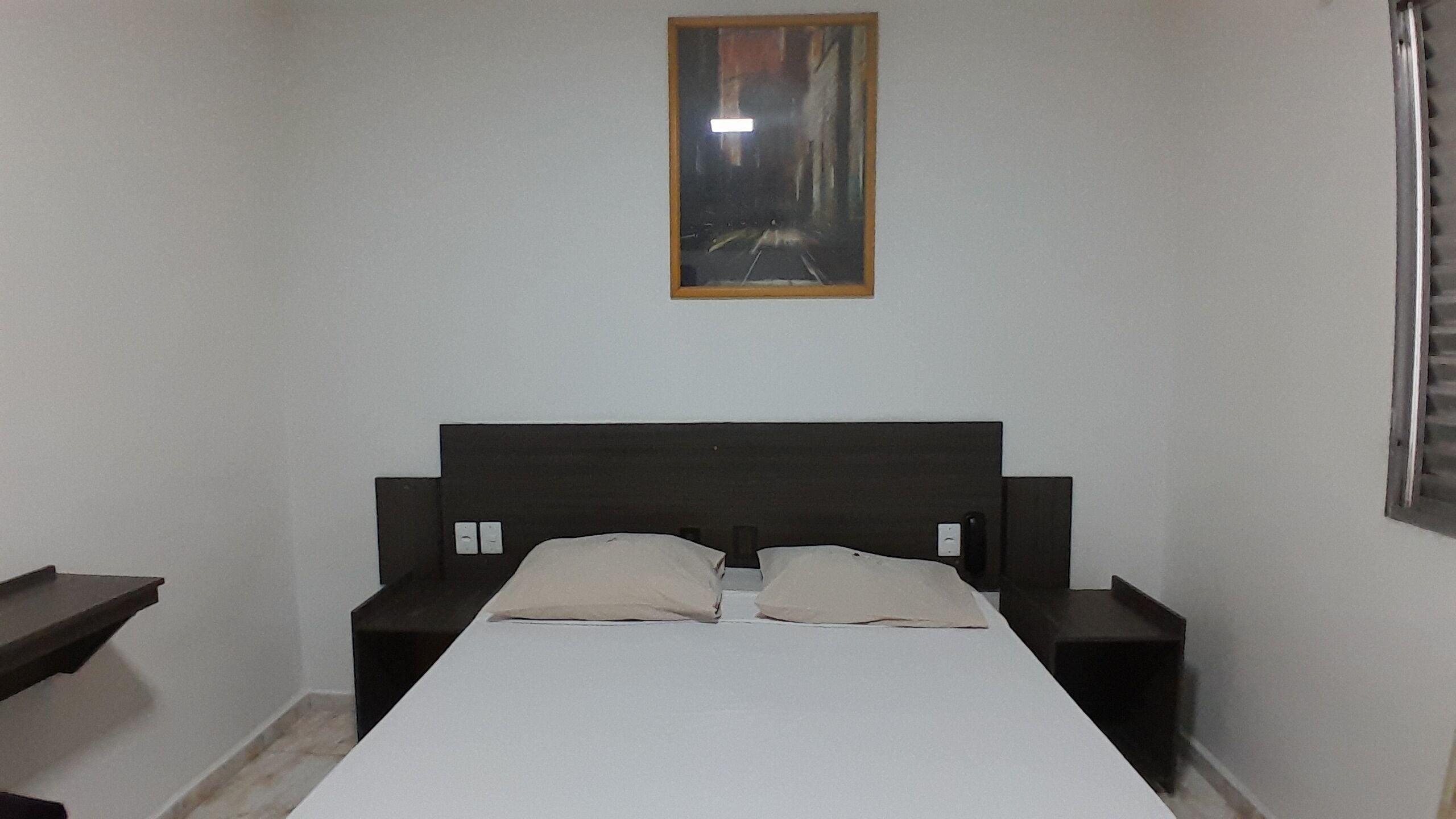 A bedroom with a single bed, two bedside tables, a nightstand, a wall-mounted light, and a framed picture above the bed.