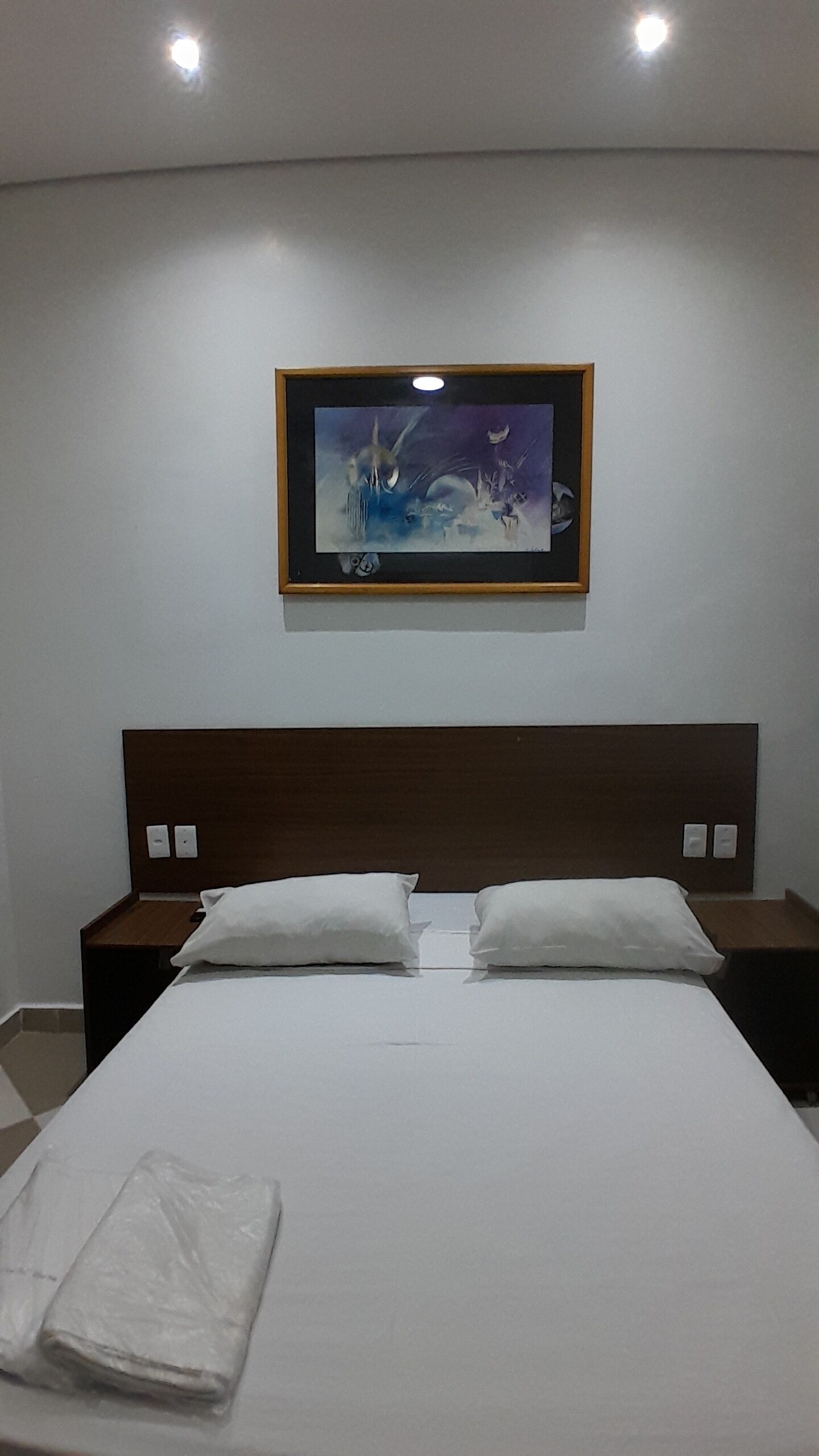 A hotel room with a large bed, two bedside tables, and a painting on the wall.