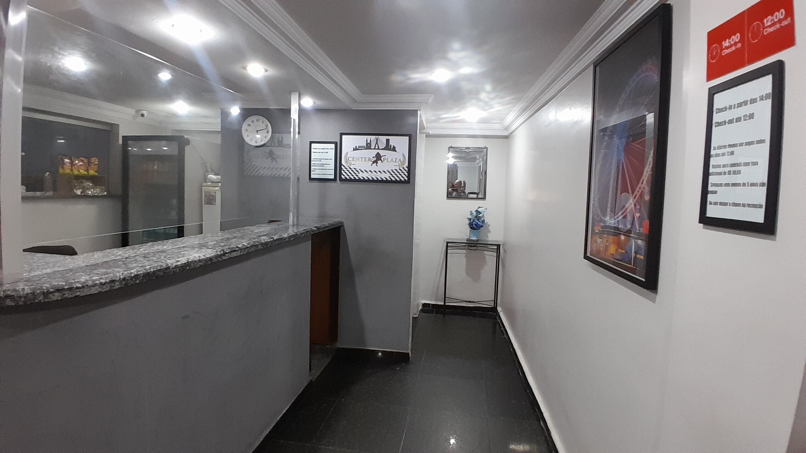 A hotel reception area with a marble counter, a clock, framed pictures, and a check-in desk.