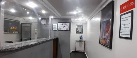A hotel reception area with a marble counter, a clock, framed pictures, and a check-in desk.