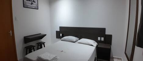 A bedroom with a bed, a nightstand, a small stool, a shelf, and a door.