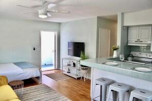 Un espace de vie compact comprenant un coin cuisine, un lit, un téléviseur et un ventilateur de plafond.