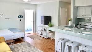 A modern kitchen with a TV, white cabinets, and a dining area with stools. - Seabreeze Suite Studio on Hollywood Beach (Hollywood)
