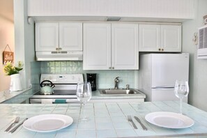 A kitchen with white cabinets, a stove, a sink, and a refrigerator. There are two wine glasses and plates on the counter.