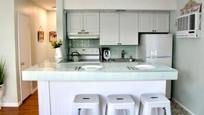 A kitchen with white cabinets, a tiled backsplash, a built-in stove, and a sink. There are two stools and a small potted plant. - Seabreeze Suite Studio on Hollywood Beach (Hollywood)