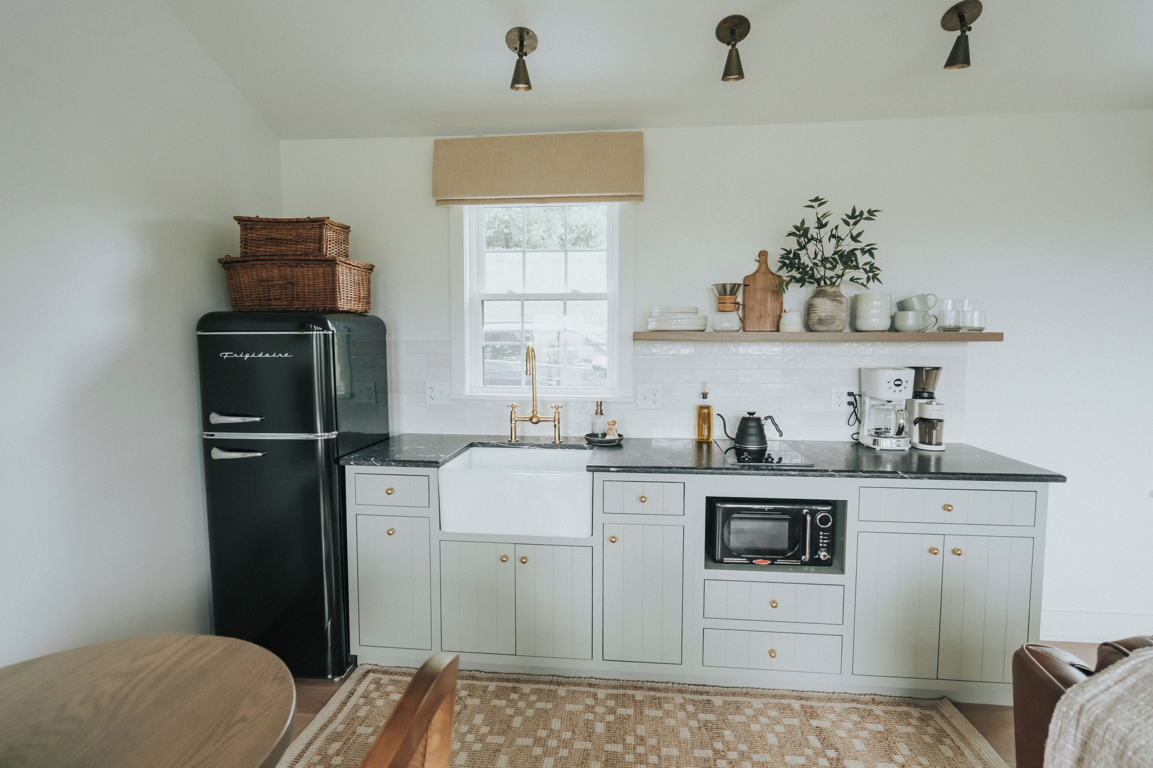 A kitchen with a black refrigerator, white cabinets, a microwave, and a window with a beige blind.