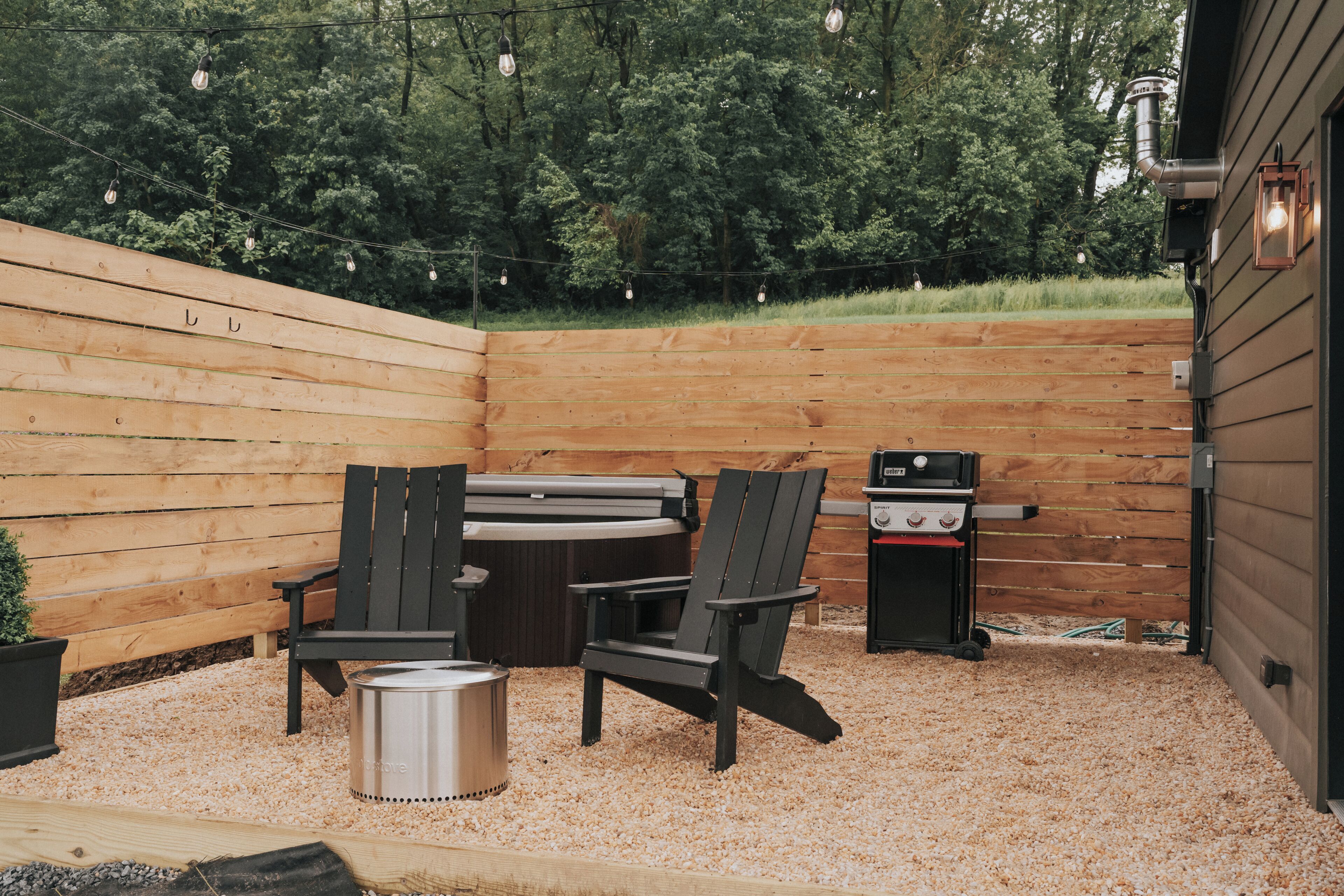 Une terrasse en bois avec des fauteuils Adirondack, un barbecue et un jacuzzi.