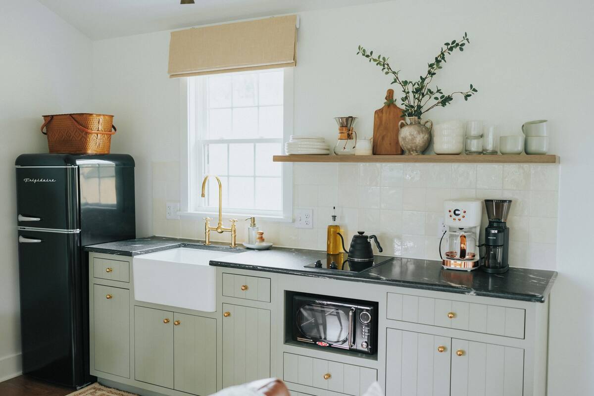 Una cocina con un refrigerador negro, un lavamanos, un microondas y una cafetera.