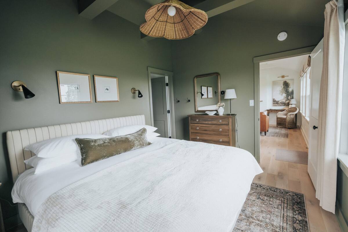 Un dormitorio con una cama grande, un aparador, un espejo y una puerta que da a otra habitación.