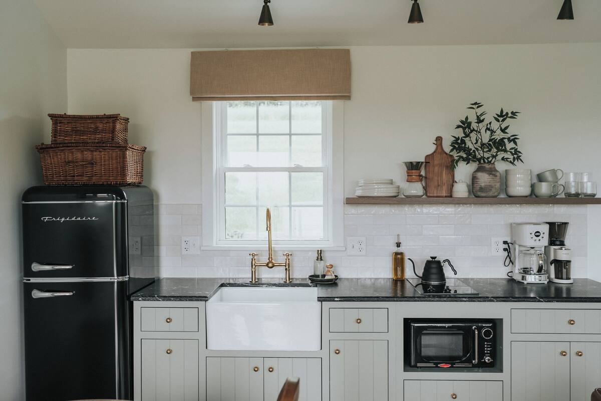 Una cocina con un refrigerador negro, gabinetes blancos, un lavamanos, un microondas y una cafetera.