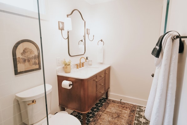 A bathroom with a toilet, sink, mirror, and a patterned rug.