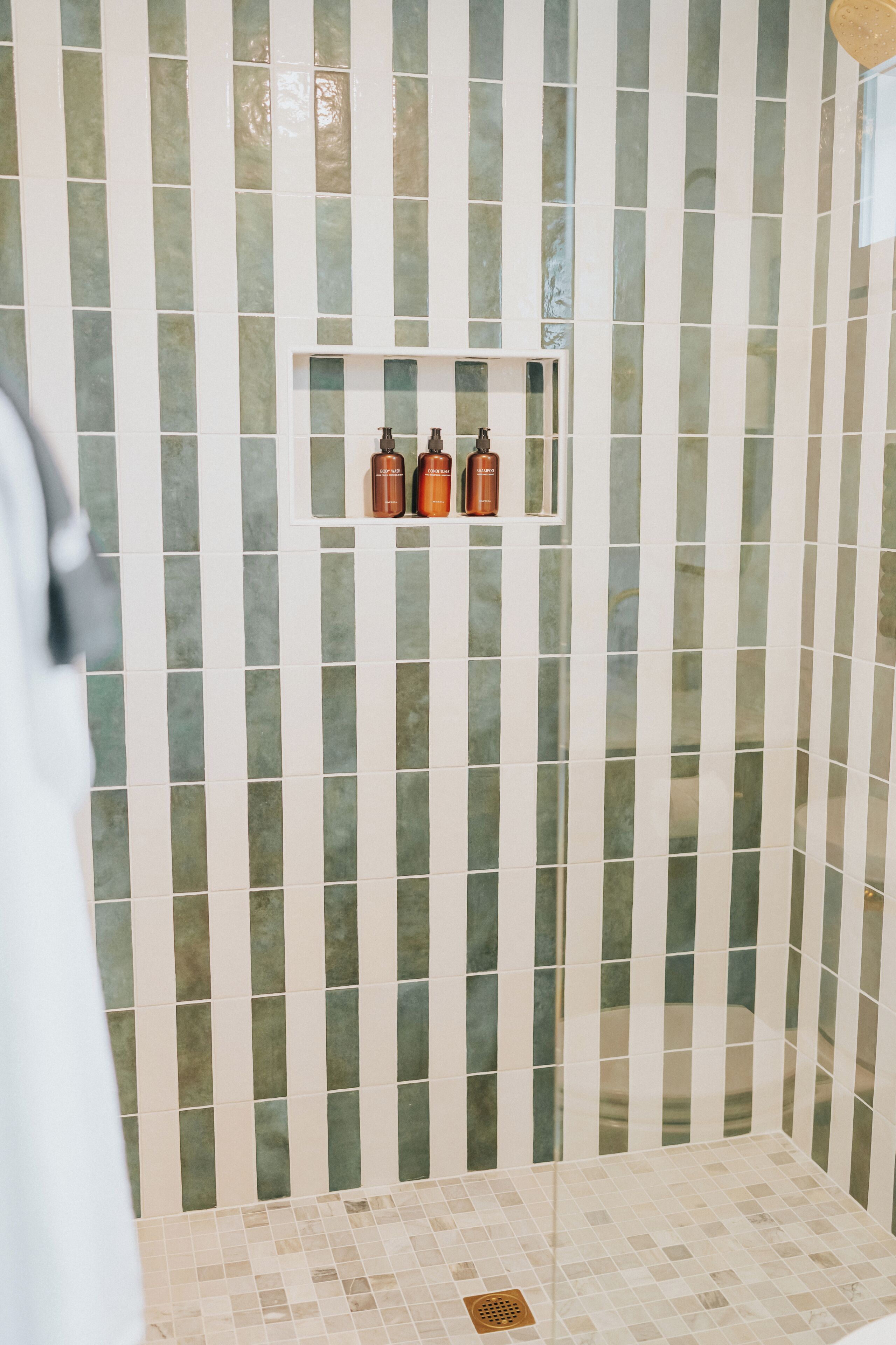A shower with vertical striped tiles and a small shelf with toiletries.