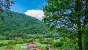 A rural landscape with a stone house, a swimming pool, and a mountain in the background.