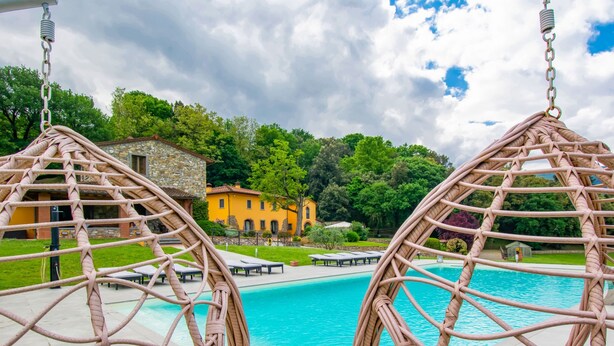 A view of a swimming pool with wicker chairs and a stone building in the background.